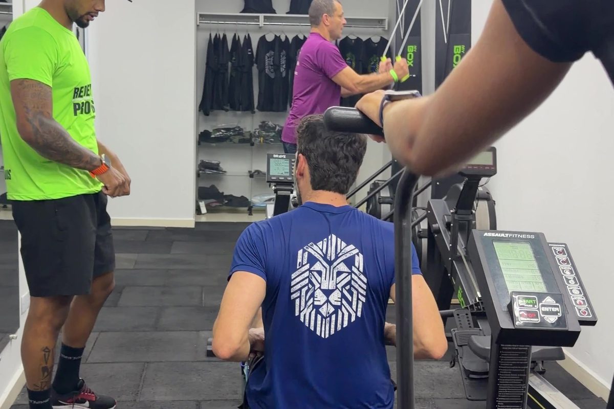 Sala de ergômetros do MyBox com professor acompanhando aluno no remo