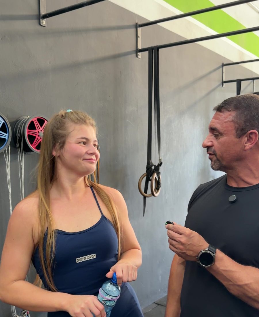 Aluna em pausa, com garrafa de água na mão, conversando com o professor dentro do box