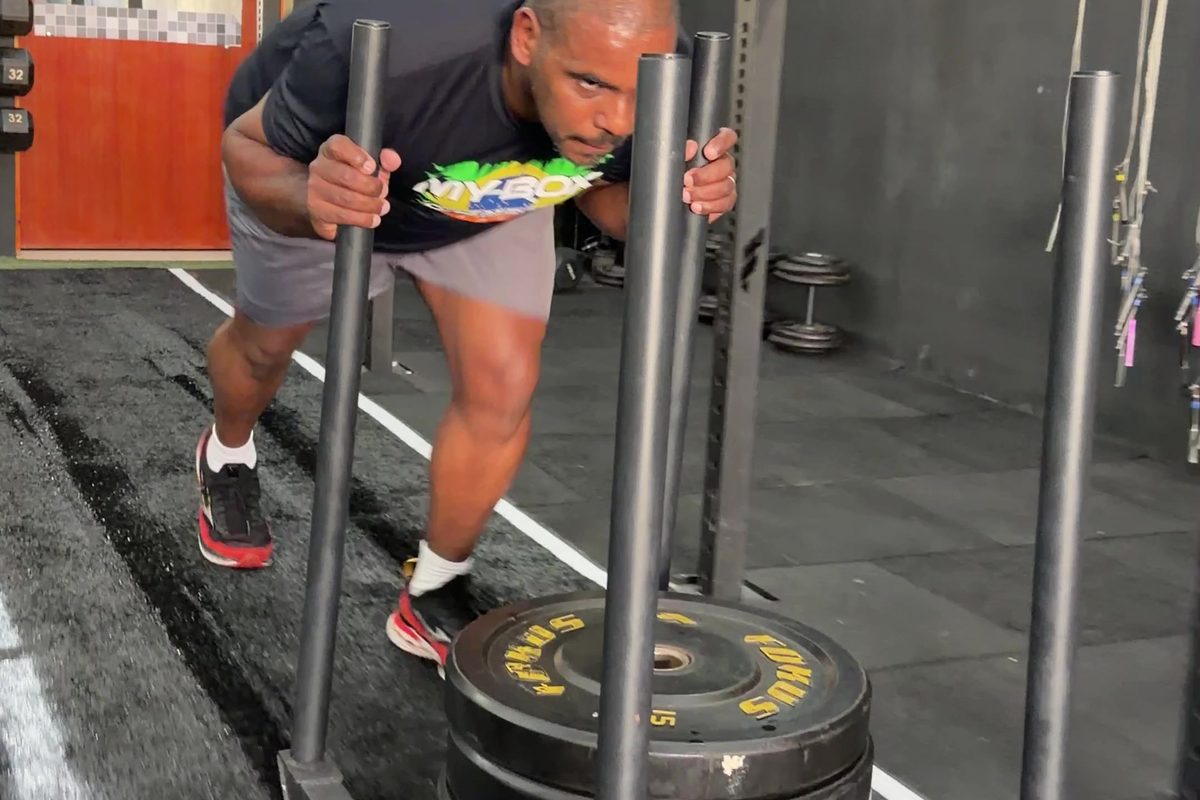 Aluno do MyBox empurrando o sled na pista de Hyrox, corpo inclinado e esforço visível